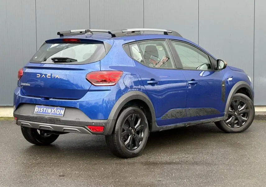 Vue 3/4 arrière droite d'une Dacia Sandero Stepway Bleu Iron avec jantes noires et barres de toit grises.