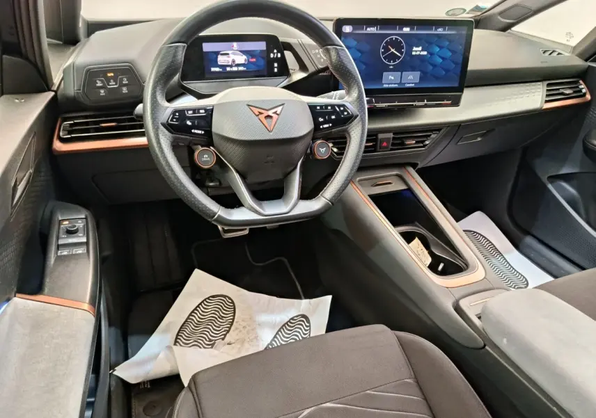 Vue intérieure avant du CUPRA Born 230ch gris foncé, avec volant multifonctions, écran tactile central et tableau de bord digital.