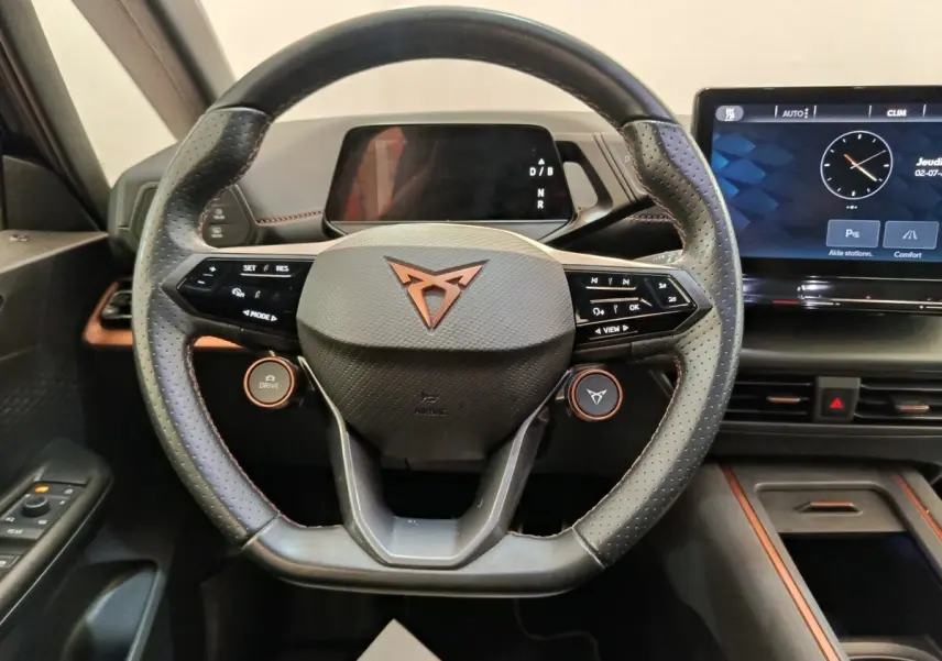 Vue intérieure centrée sur le volant noir perforé avec logo CUPRA cuivré et écran tactile du tableau de bord.