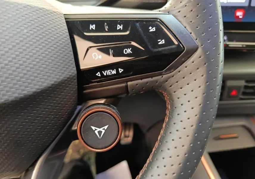 Gros plan sur le volant cuir perforé avec commandes tactiles et logo CUPRA sur molette en aluminium cuivré.