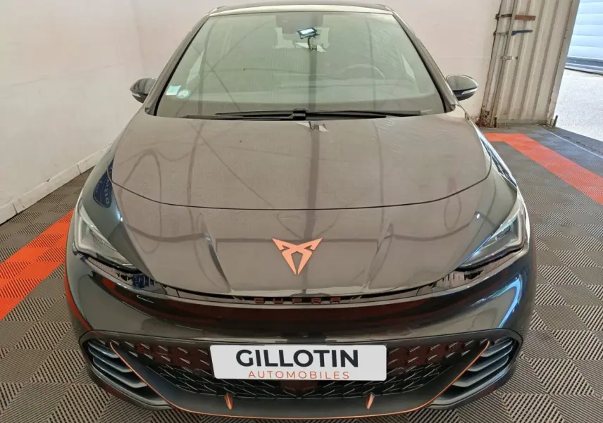 Vue avant plongeante d'une CUPRA BORN gris foncé avec logo cuivré et calandre noire ajourée dans un garage.