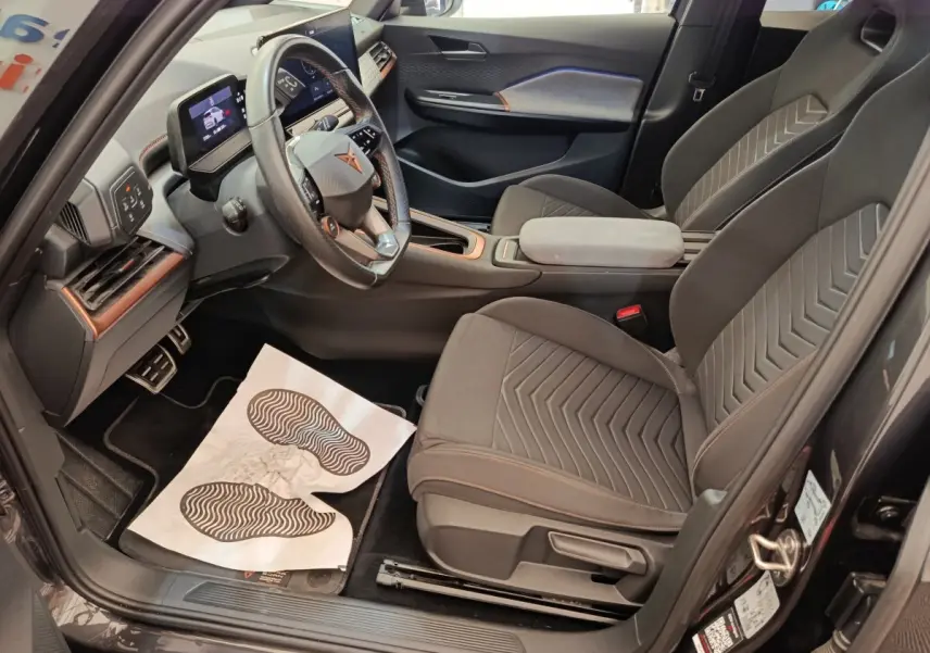 Intérieur avant droit du CUPRA Born gris foncé 2023, volant cuir multifonctions et sièges tissu avec surpiqûres orange.