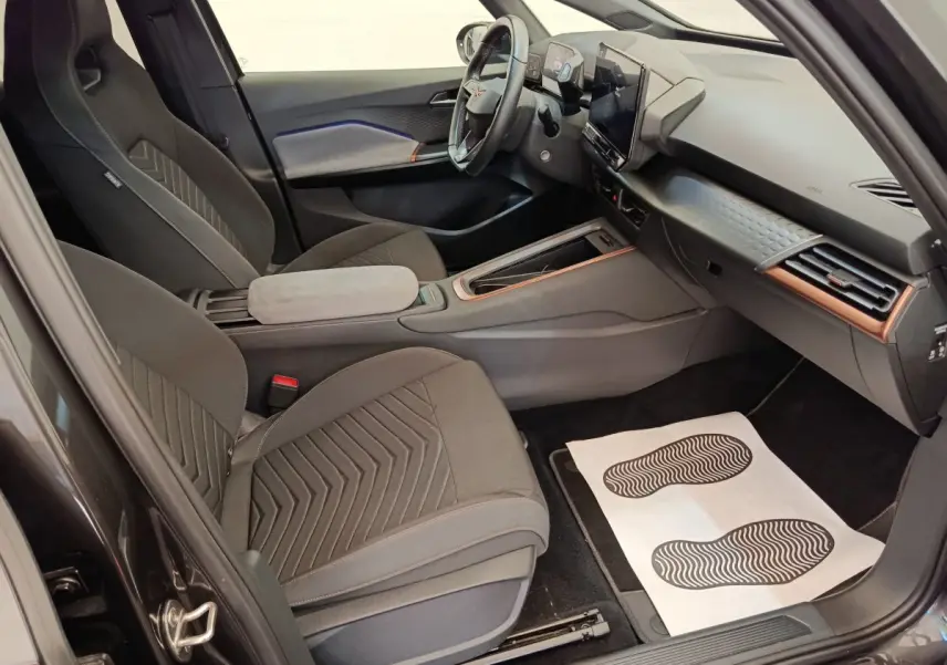 Intérieur avant droit de la CUPRA BORN gris foncé 2023, avec tableau de bord moderne et sièges en tissu noirs.