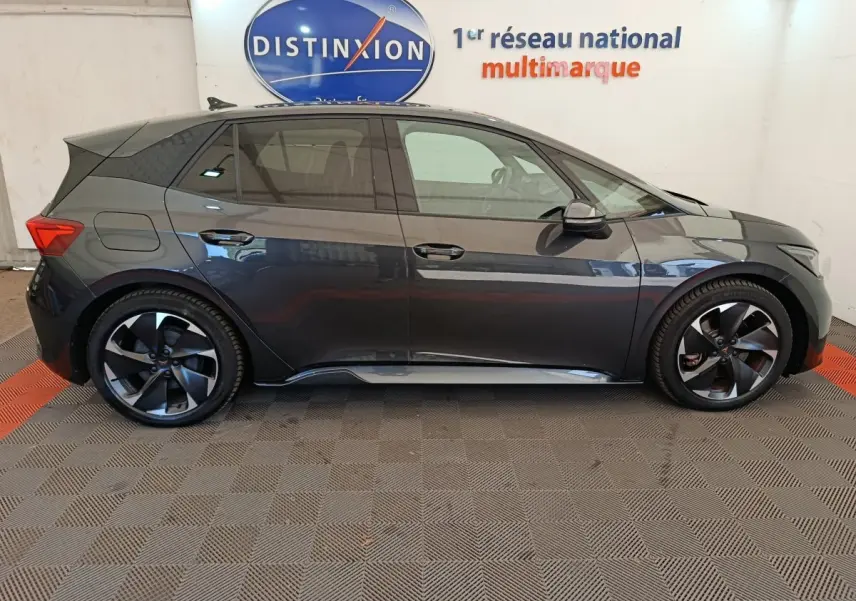 Vue de profil côté gauche d'une CUPRA BORN gris foncé 2023 avec jantes noires et toit noir dans un showroom.