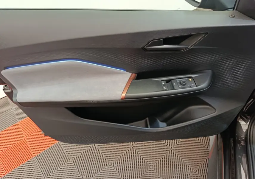 Vue rapprochée de la porte avant gauche du CUPRA Born gris foncé, avec habillage tissu clair et éclairage d'ambiance bleu.