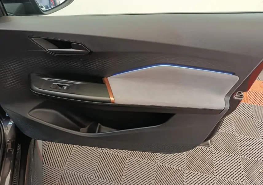 Vue intérieure côté gauche de la porte d’une CUPRA BORN gris foncé, avec éclairage d’ambiance bleu et garniture bicolore.