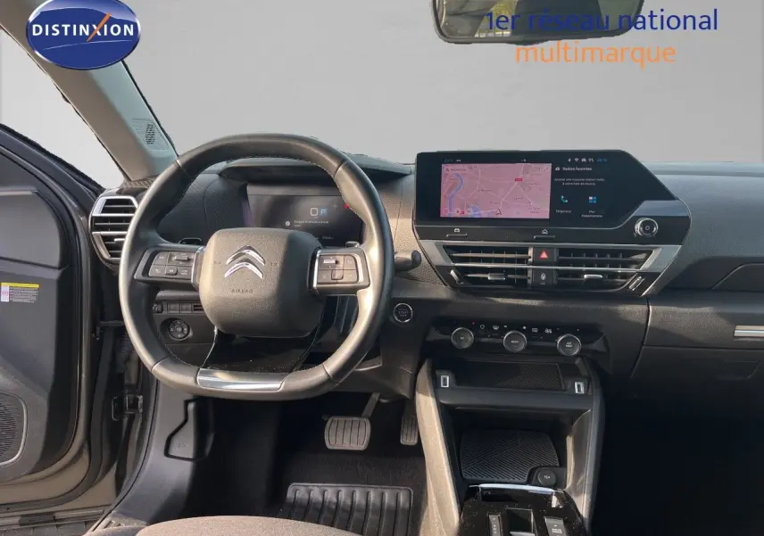 Vue intérieure avant centrée sur le volant et le tableau de bord noir du Citroën C4 gris 2023 avec écran tactile et commandes intégrées.