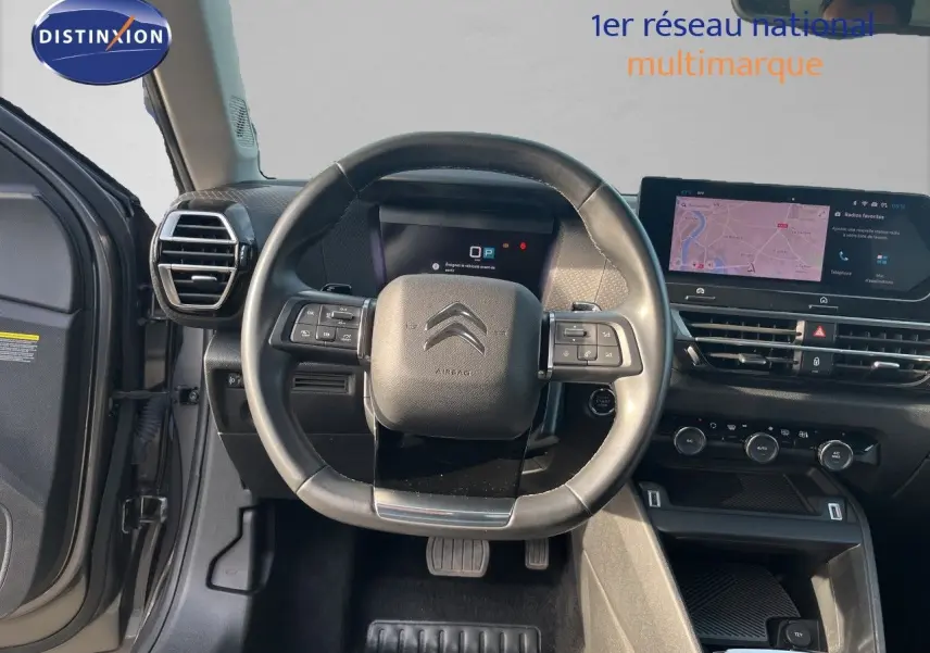 Vue intérieure centrée sur le volant noir d'une Citroën C4 2023 avec tableau de bord digital et écran tactile.