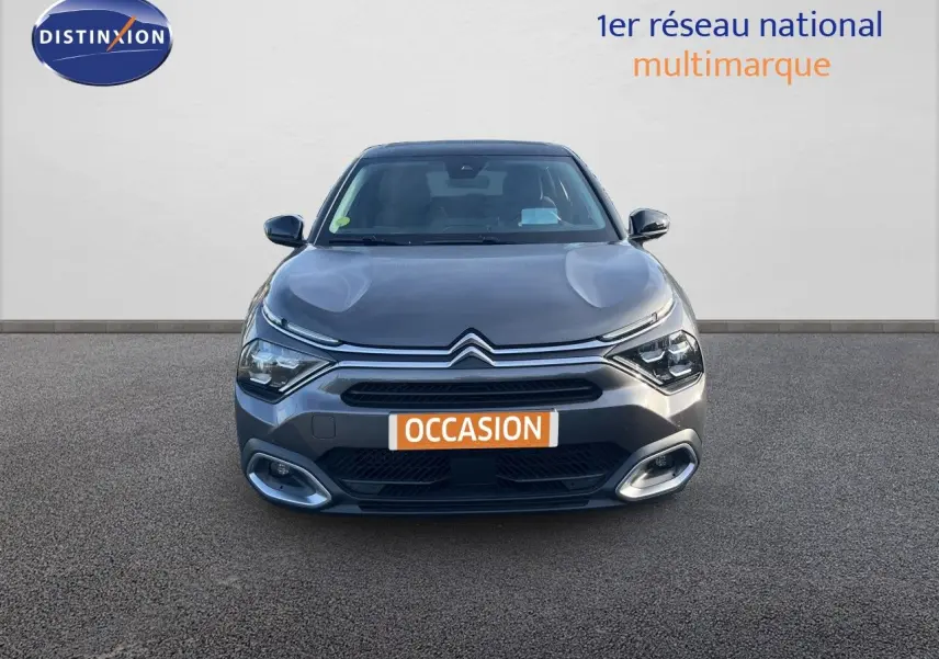 Vue frontale d'une Citroën C4 gris métallisé 2023 avec calandre distinctive et feux LED allumés.