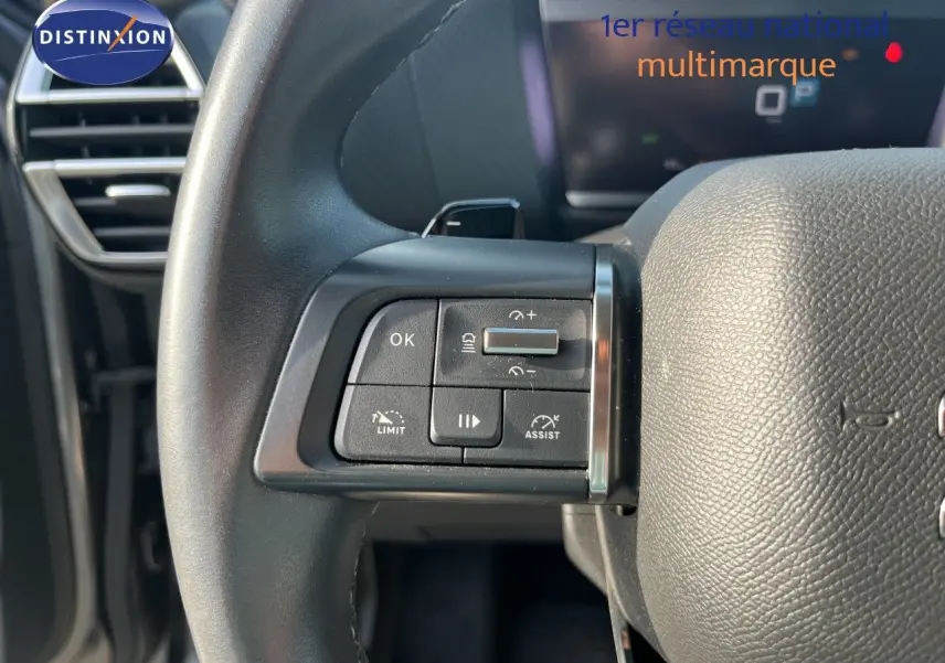 Gros plan sur les commandes à gauche du volant noir d'une Citroën C4 gris 2023, avec tableau de bord numérique en arrière-plan.