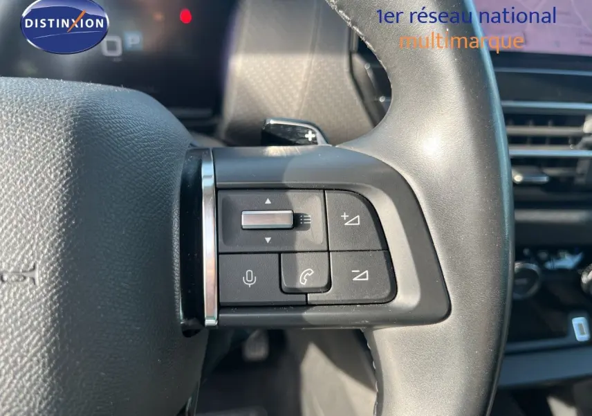 Gros plan sur les commandes au volant côté gauche du Citroën C4 gris 2023, avec boutons de volume et téléphone.