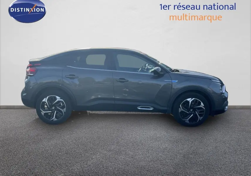 Profil droit d'une Citroën C4 2023 gris métallisé avec jantes noires et détails chromés sous un mur blanc.