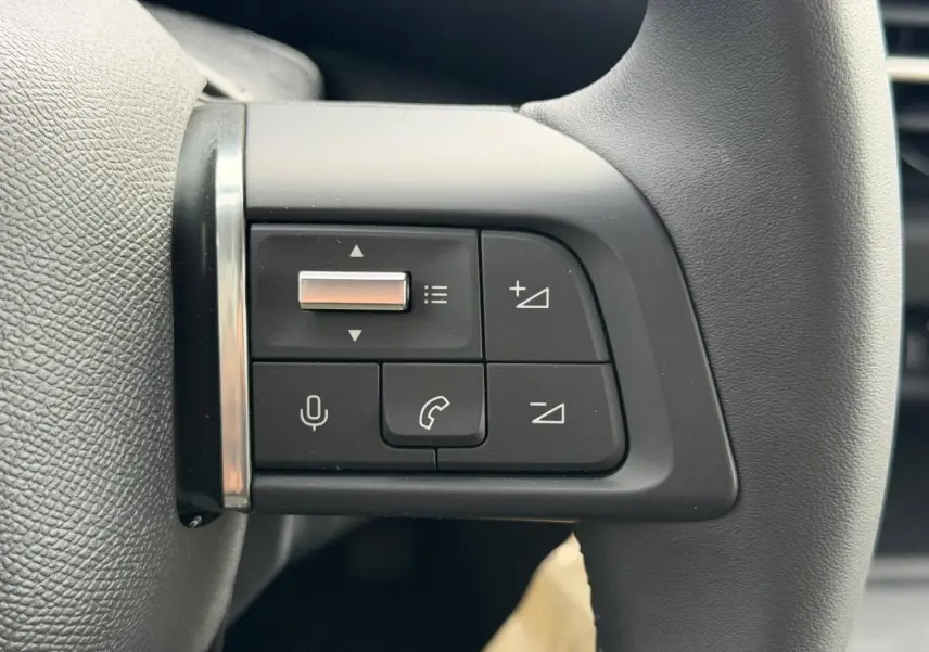 Gros plan sur les commandes audio et téléphone intégrées au volant noir de la Citroën C4 électrique 2024.