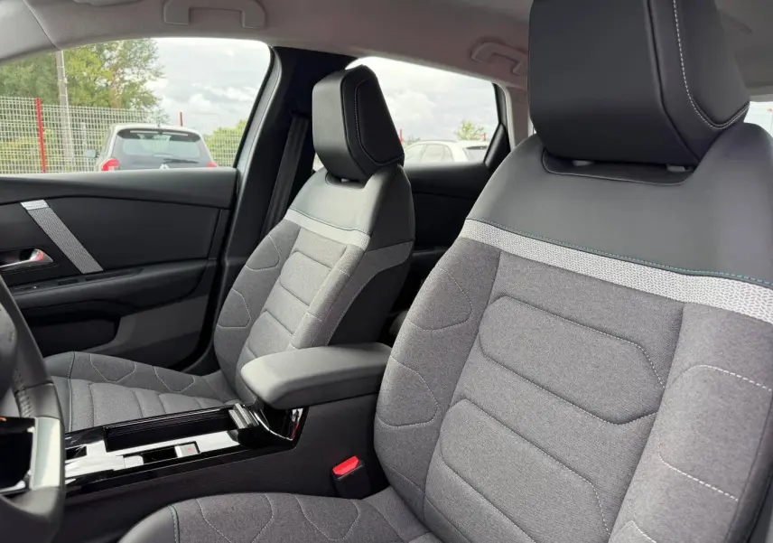 Vue intérieure des sièges avant gris et noir avec surpiqûres blanches de la Citroën C4 électrique 2024, côté conducteur.