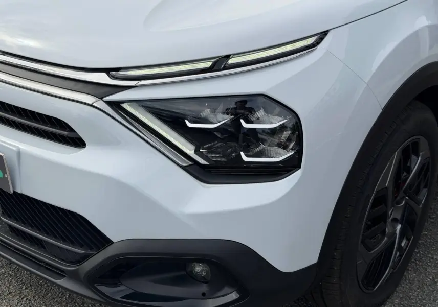 Gros plan sur l’avant droit blanc du Citroën C4 électrique 2024, mettant en valeur les phares LED et la roue noire.