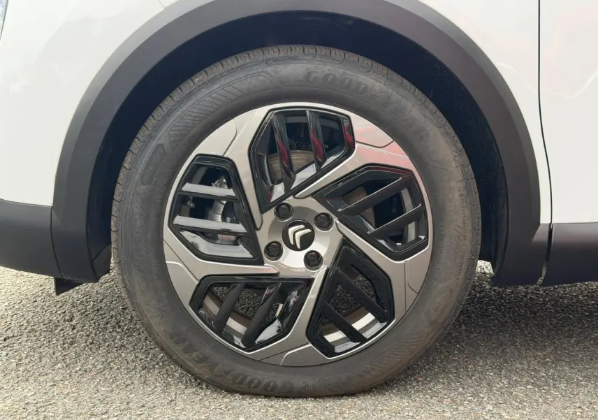 Gros plan sur la roue avant droite blanche d'une Citroën C4 électrique 2024 avec jante au design géométrique noir et argent.
