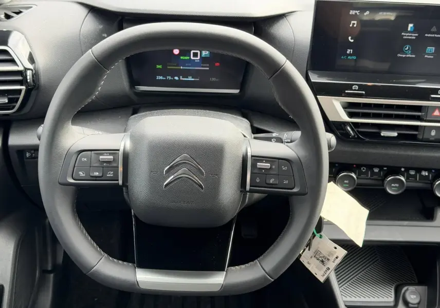 Vue rapprochée du volant noir et du tableau de bord numérique de la Citroën C4 électrique blanche 2024.