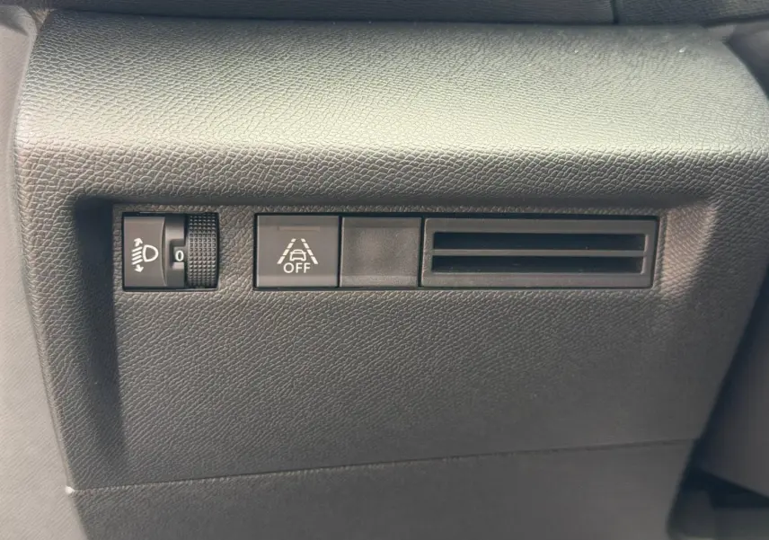 Détail du tableau de bord noir avec commande de réglage des phares, bouton d'alerte et prise d'air sur Citroën C4 électrique.