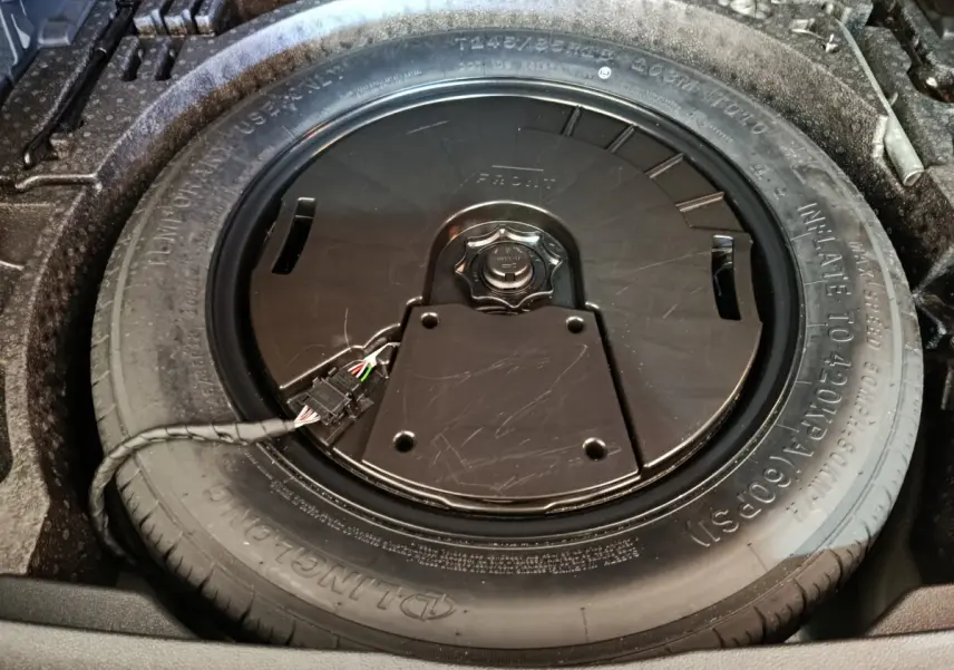 Gros plan sur la roue de secours dans le coffre du Volkswagen Tiguan noir, montrant le pneu et son boîtier central.
