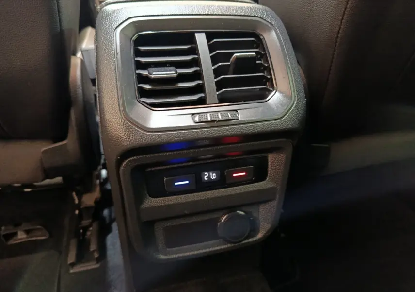 Vue rapprochée de la console centrale arrière noire du Volkswagen Tiguan 2.0 TDI avec commandes de climatisation et prise 12V.