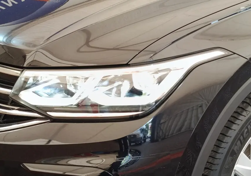 Gros plan sur le phare avant droit allumé d’un Volkswagen Tiguan noir, soulignant la calandre chromée et la carrosserie brillante.