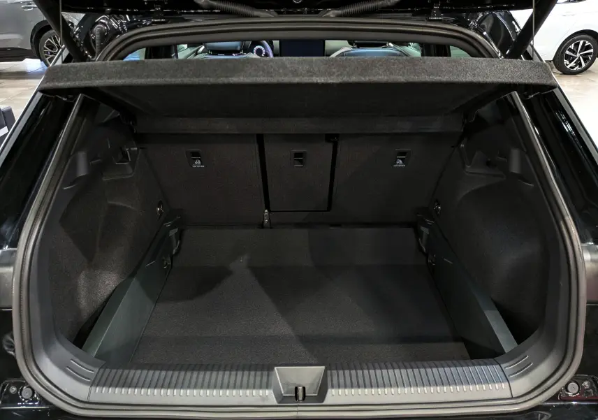 Coffre ouvert vu de l'arrière d'un Volkswagen T-Roc eTSI 150 CH DSG7 R-Line noir Ébène, intérieur spacieux et habillage sombre.