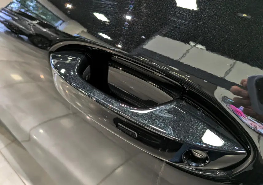 Gros plan sur la poignée de porte noire ébène du Volkswagen T-Roc eTSI 150 CH DSG7 R-Line 2026, finition brillante.