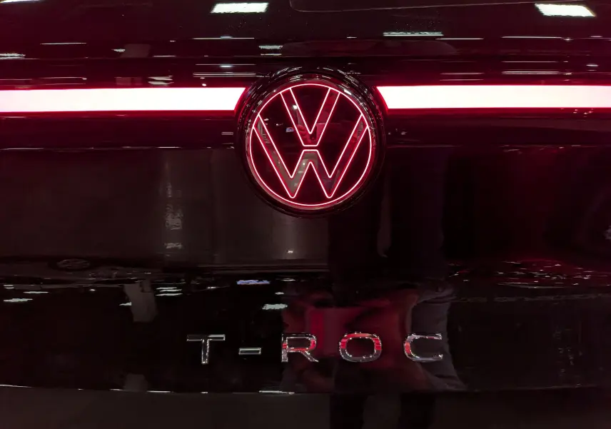 Gros plan sur le logo Volkswagen illuminé en rouge et le nom T-ROC sur la malle arrière noire Ébène du SUV.