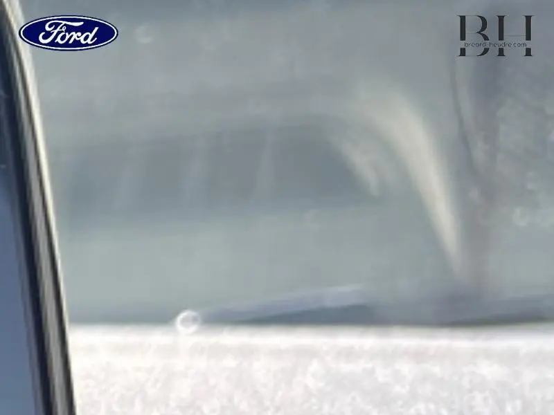 Gros plan sur la vitre latérale gauche d'une Ford Fiesta bleu azur métallisée avec reflet flou de l'habitacle.