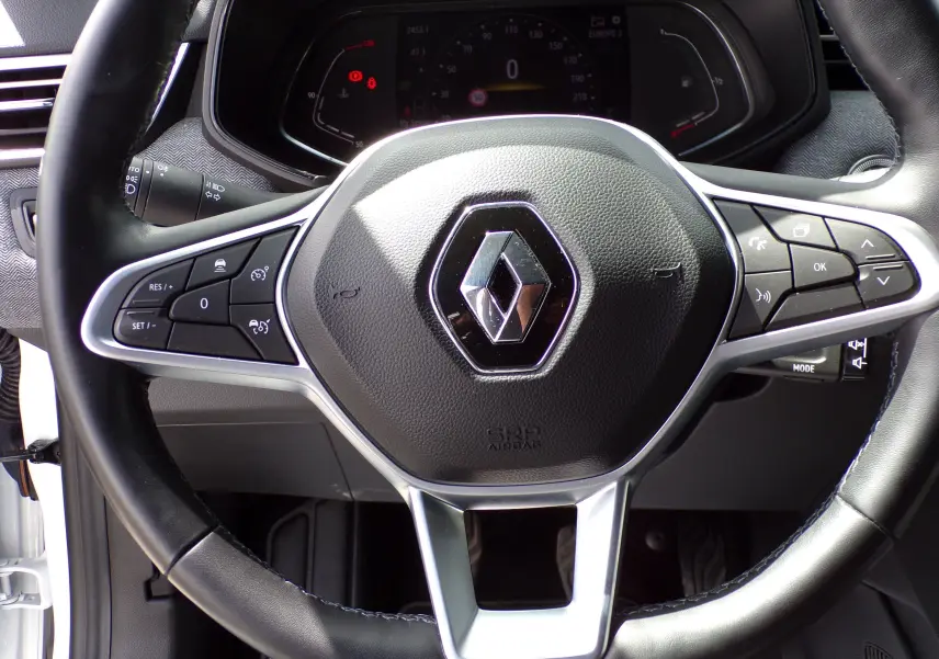 Gros plan sur le volant cuir noir de la Renault Clio V 1.3 TCE 140 ch blanc avec commandes multifonctions intégrées.