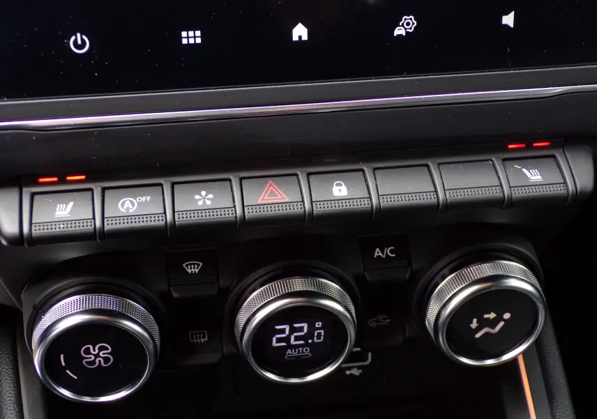 Gros plan sur la console centrale de la Renault Clio V blanche, montrant les commandes de climatisation et les boutons de fonction.