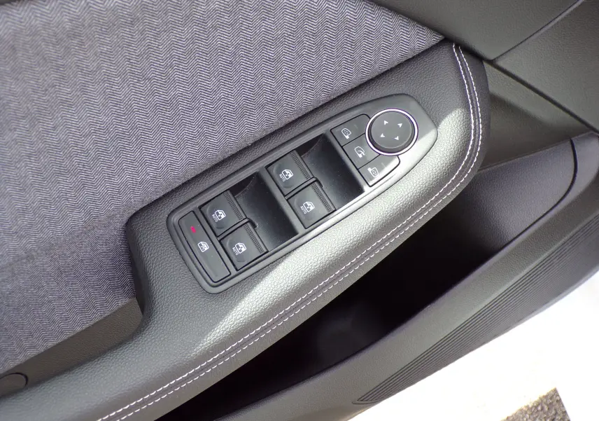 Gros plan sur les commandes de lève-vitres et réglage des rétroviseurs sur la porte côté gauche d'une Renault Clio V blanche.