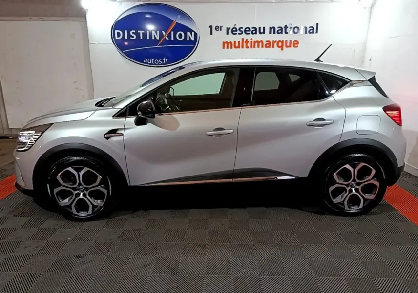 Profil droit d’un Renault Captur Intens E-Tech hybride rechargeable gris clair, avec jantes distinctives et vitres teintées.