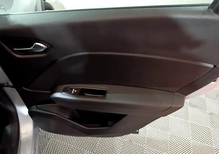 Vue intérieure du panneau de porte côté gauche du Renault Captur gris clair, avec poignée et commande de vitre électrique.