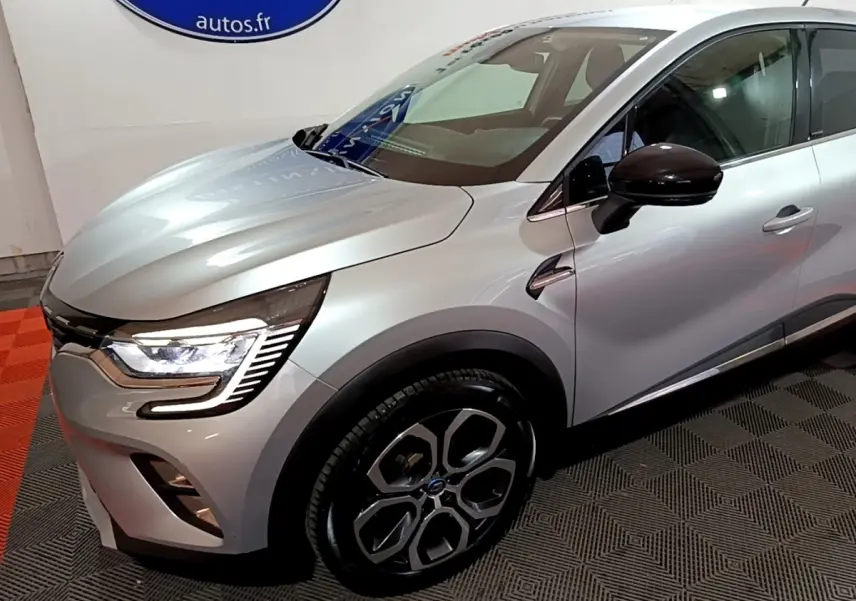 Vue 3/4 avant droit d’un Renault Captur Intens E-Tech hybride rechargeable gris clair avec phares LED et jantes distinctives.