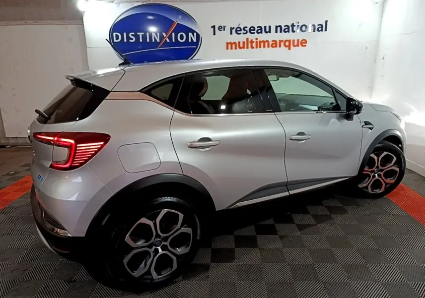 Vue latérale droite d’un Renault Captur Intens E-Tech hybride rechargeable gris clair avec feux arrière LED allumés en intérieur showroom.