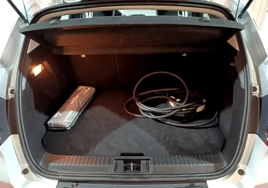 Coffre ouvert vu de l'arrière d'un Renault Captur gris clair avec câble de recharge et trousse de secours visible.