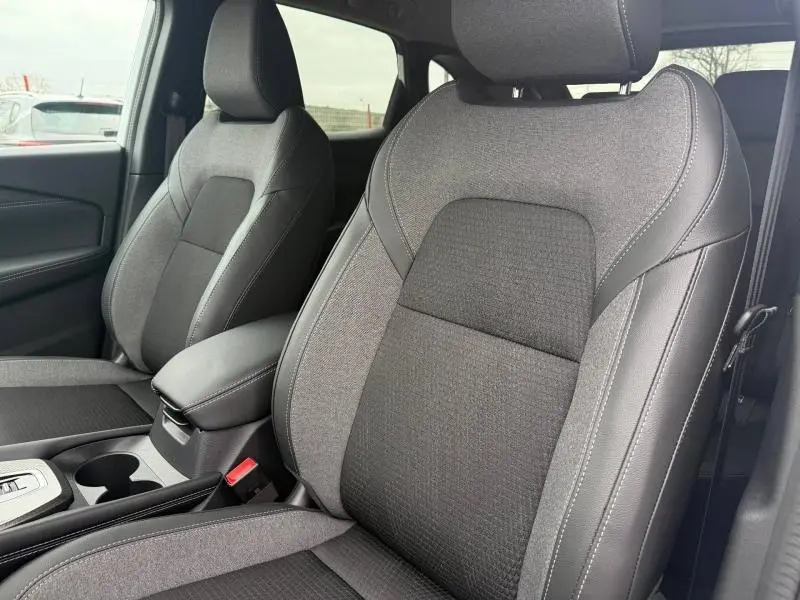 Vue intérieure rapprochée des sièges avant gris et noir du Nissan Qashqai Hybrid e-POWER 2025, avec accoudoir central.