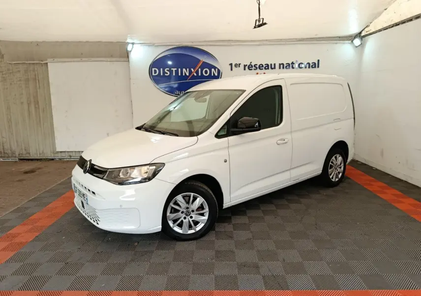 Vue 3/4 avant droit d'un Volkswagen Caddy blanc 2022 avec jantes alliage et rétroviseurs noirs dans un garage.