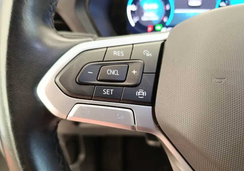 Gros plan sur les commandes du volant cuir noir du Volkswagen Caddy blanc, avec boutons multifonctions et régulateur de vitesse.