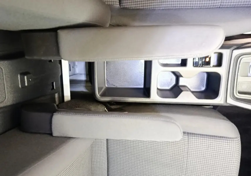 Vue intérieure rapprochée du Volkswagen Caddy 2022 montrant l'accoudoir central et les porte-gobelets entre les sièges avant.
