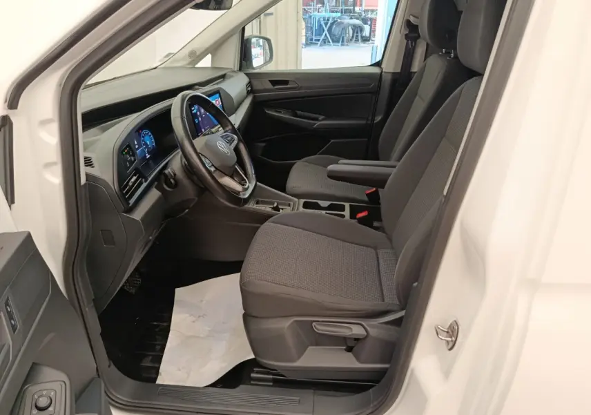 Vue intérieure côté conducteur du Volkswagen Caddy blanc 2022, avec tableau de bord numérique et volant cuir multifonctions.