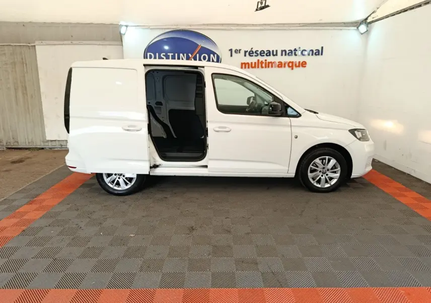 Vue de profil côté droit du Volkswagen Caddy blanc 2022 avec porte coulissante arrière ouverte en intérieur showroom.