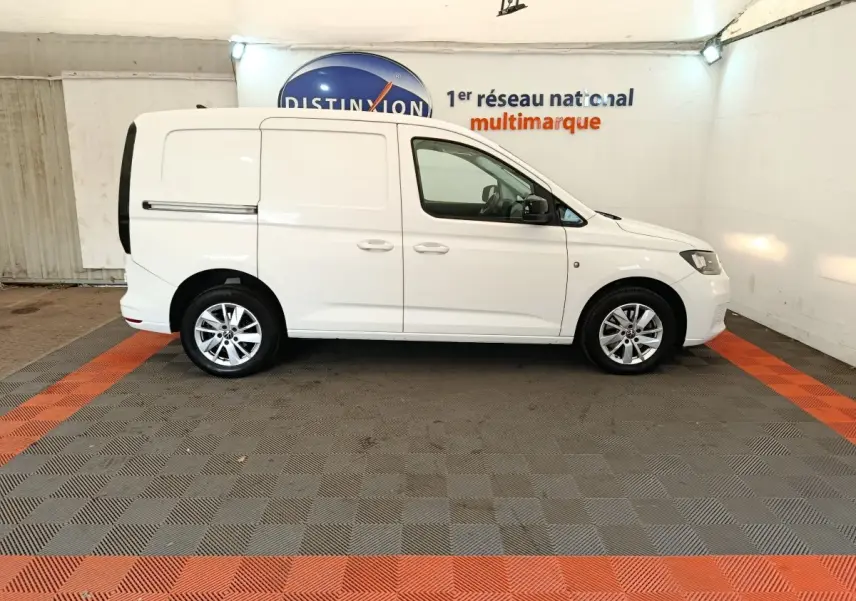 Vue de profil côté droit d'un Volkswagen Caddy blanc 2022 en intérieur sur sol gris et orange.