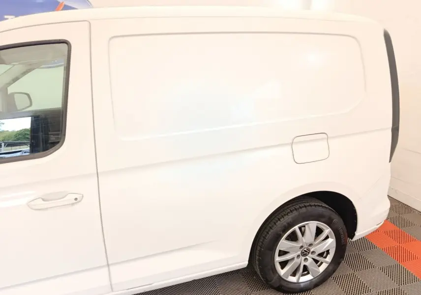 Vue latérale droite du Volkswagen Caddy blanc, mettant en valeur la porte latérale et la roue arrière avec jante alliage.