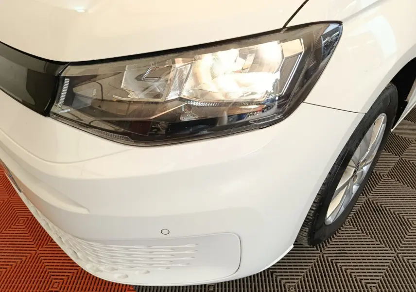 Gros plan sur l'avant droit blanc d'un Volkswagen Caddy 2022, mettant en valeur le phare et la roue.