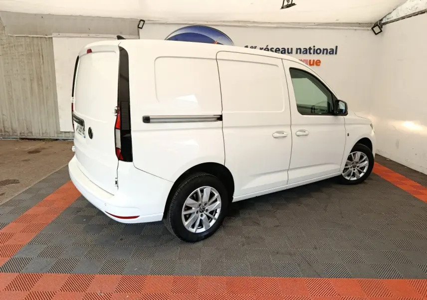 Vue 3/4 arrière droite d'un Volkswagen Caddy blanc, fourgon utilitaire avec jantes alliage et portes latérales pleines.