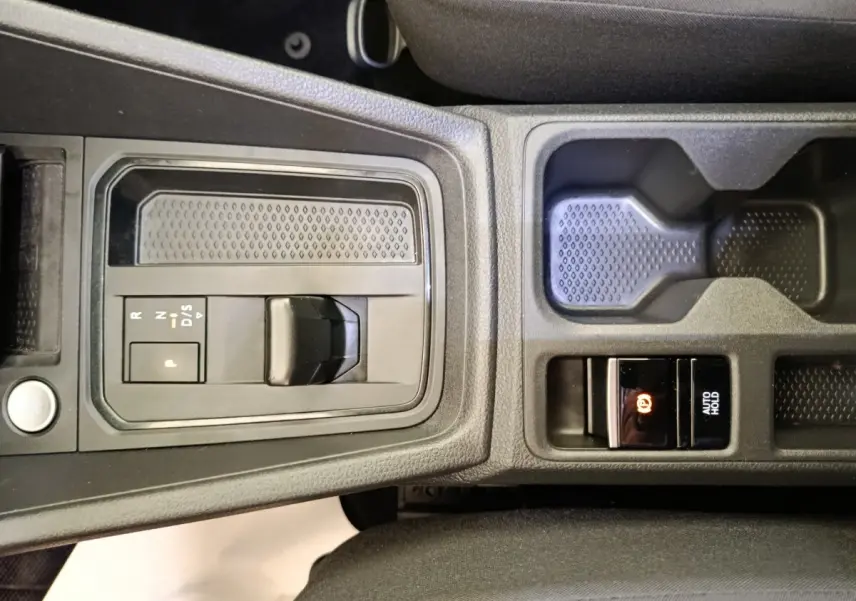 Vue rapprochée de la console centrale noire du Volkswagen Caddy 2022, avec levier de boîte auto et frein à main électrique.
