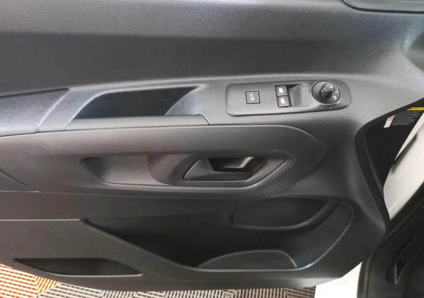Vue rapprochée de la porte intérieure côté conducteur du Peugeot Partner blanc, avec commandes de vitres et rétroviseur.