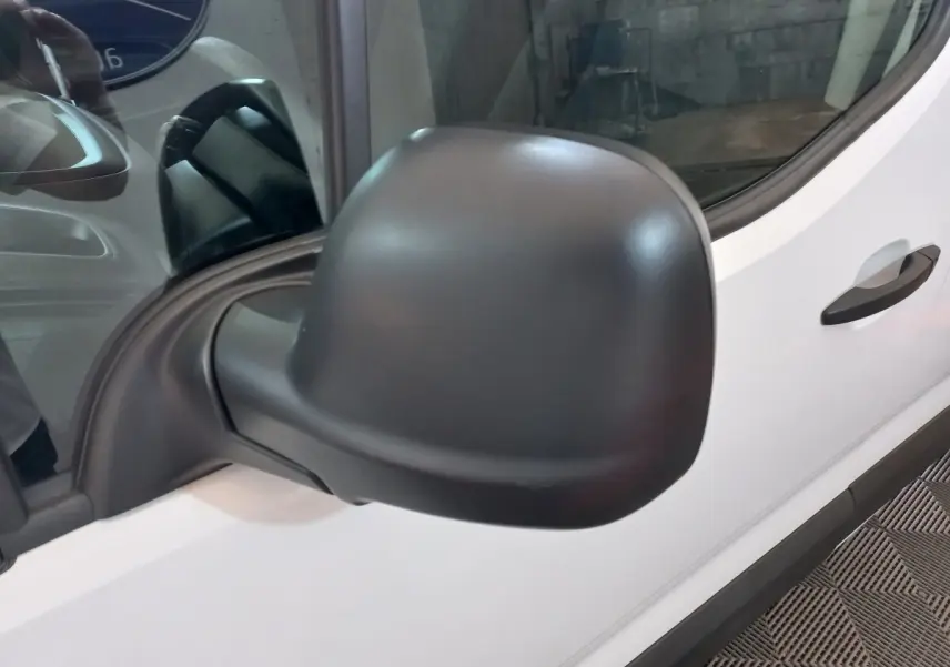 Gros plan sur le rétroviseur côté conducteur noir d’un Peugeot Partner blanc, vue latérale avant droite.